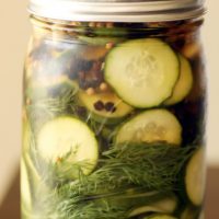 The top half of a glass mason jar full of cucumber pickles and other greens