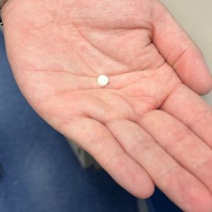 hand holding a small white oral insulin tablet
