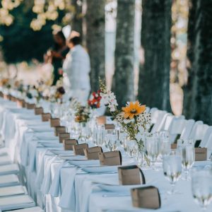A beautiful long table dinner place setting with white tablecloths and poplar trees in the background
